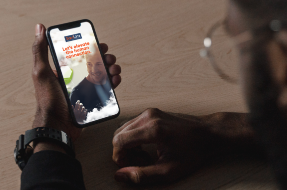 A man leaning on a table looks at the SaviLinx website on his smartphone.